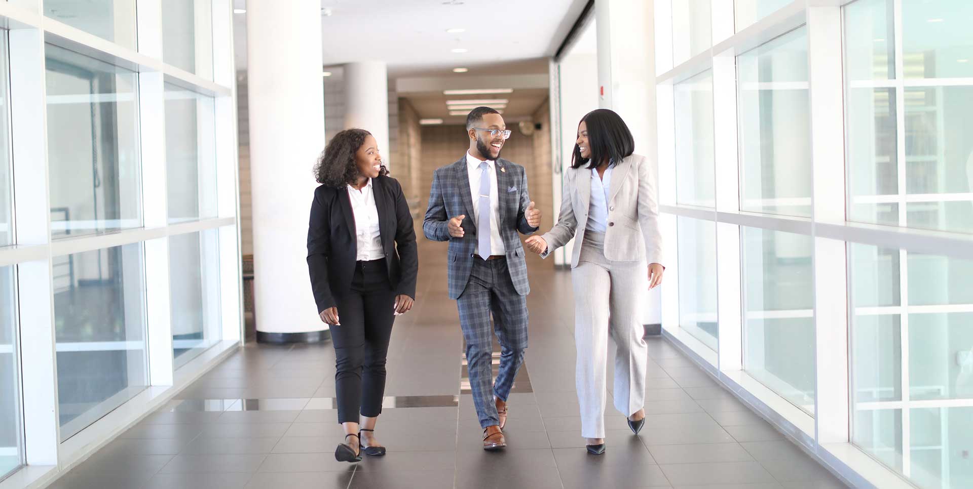 business students 2 female, one male, walk and talk in hallway