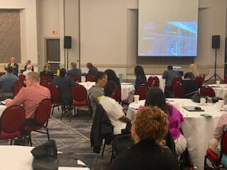 Particpants in the 2024 Faculty Enrichment Workshop seated at tables and looking at a projection screen